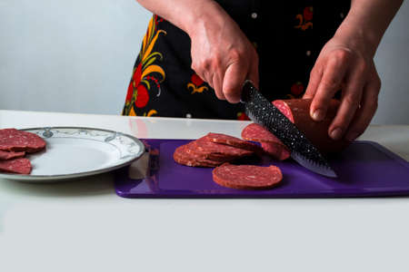 Slicing a sausage loaf with a black knife.の写真素材