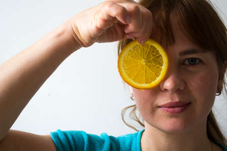 Instead of an orange slice of eye. The girl holds an orange on a white background.の写真素材