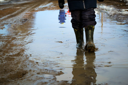 A boy in rubber boots walks through a puddle. Spring slush.