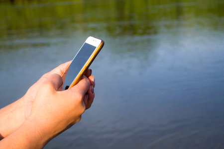 Hand Holding Cellphone With Blank Screen Showing Mobile App Against Sea Beach Outdoor. Cropped,...