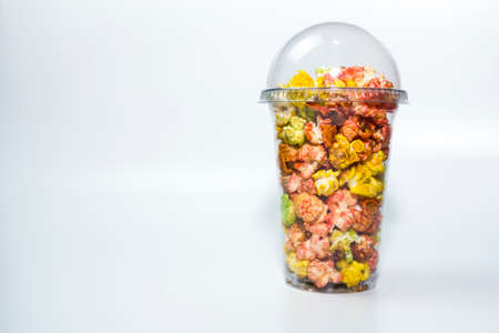 Colorful popcorn in a transparent cup on a white background, ready to watch a movie.の写真素材