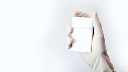 A hand in a medical glove holds a white pack of cigarettes, an anti-smoking concept.の写真素材