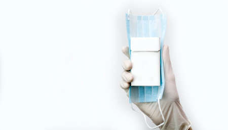 A gloved hand holds a mask and a pack of cigarettes, smoking or mask is your choice.の写真素材