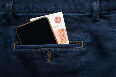 Banknotes of five thousand Russian rubles in the back pocket of jeans, along with a phone. Shopping. Telephone communications.の写真素材