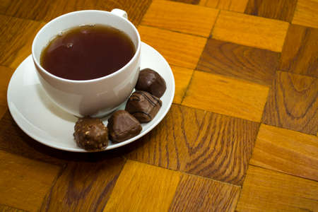 A white cup of hot tea and sweets on a saucer and all this stands on a wooden table.の写真素材