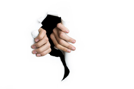 The fingers of the hands tear a hole on a white background.の写真素材