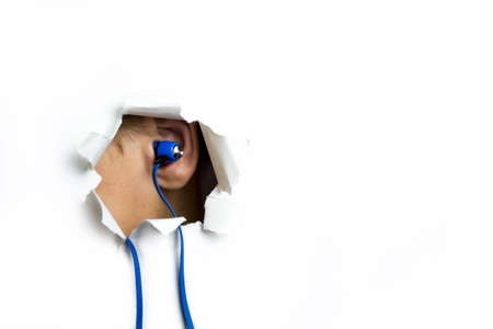 Blue headphones in my ear stick out through a hole on a white background.の写真素材