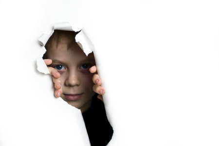 A boy peeks out of a hole on a white background.の写真素材