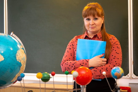 The teacher stands near the blackboard with a folder in his hands.