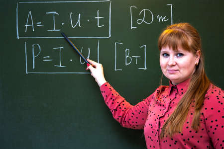 A physics teacher stands near the blackboard where formulas for physics are written.の写真素材