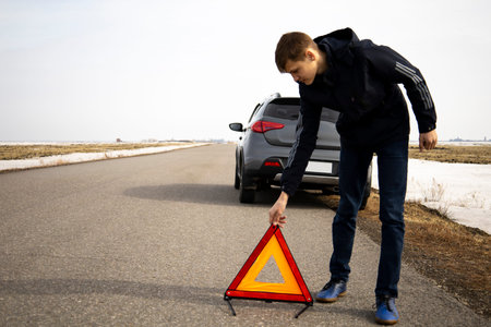 a male driver puts a red triangle warning sign on the road as a symbol of a car breakdown