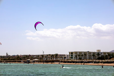 A person is joyfully flying a colorful kite high over a shimmering body of water on a beautiful, sunny dayの写真素材