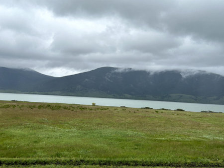 A serene lake with majestic mountains towering in the background and a lush grassy field stretching out in the foregroundの写真素材