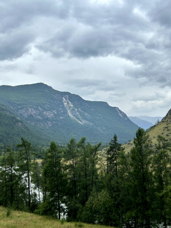 This is a breathtaking view of a majestic mountain range, featuring lush trees in the foreground and a tranquil river flowing in the backgroundの写真素材
