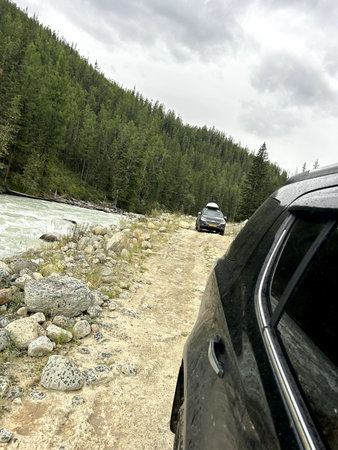 A car is steadily driving down a bumpy dirt road that runs alongside a sparkling river, creating a...