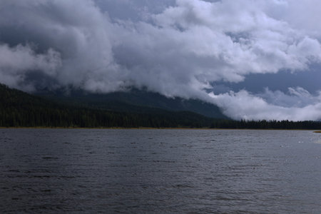 A serene lake scene under a dramatic sky, where dark clouds loom over the mountains, creating a captivating and moody atmosphere.の写真素材
