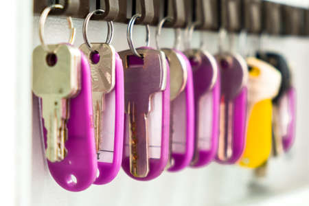 Keys with multi-colored tags hang in the wall box for storing the keys, close-up.の写真素材