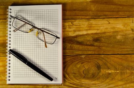 Fountain pen, glasses, and notebook on a wooden tableの写真素材