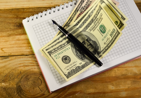 Notebook with fountain pen and banknotes on a wooden tableの写真素材