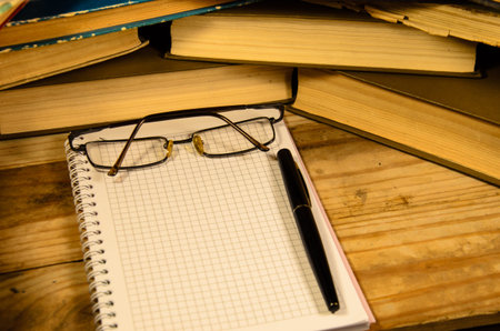 Notepad, fountain pen and glasses in front of many books