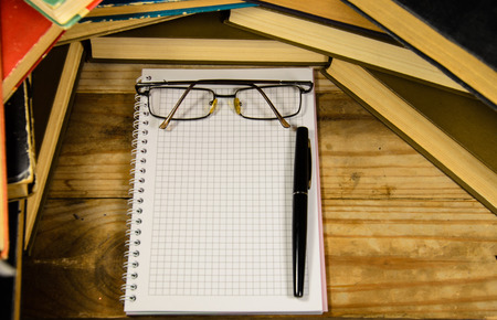 Notepad, fountain pen and glasses in front of many booksの写真素材