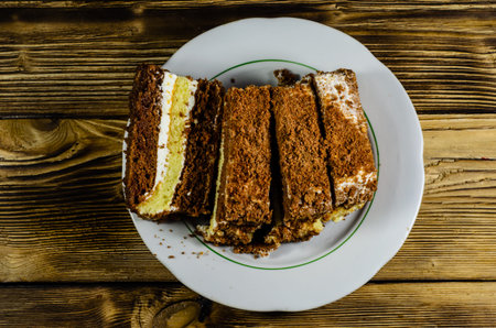 Sliced biscuit cake in plate on wooden table. Top view