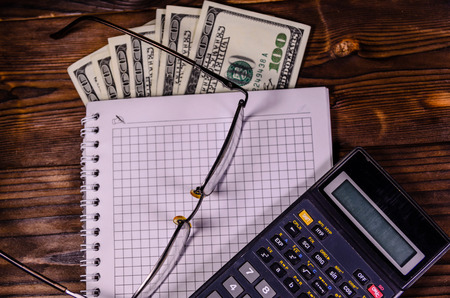 Notepad, pen, calculator and dollar bills on rustic wooden table. Top viewの写真素材