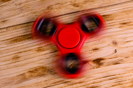 Red fidget spinner rotates on rustic wooden deskの写真素材