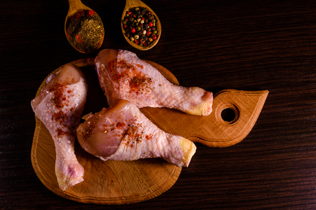 Chicken legs with different spices on wooden cutting board. Top viewの写真素材