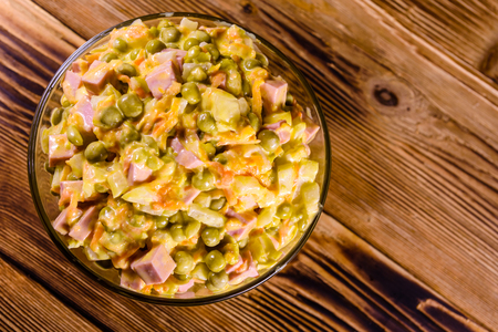 Salad with sausage, green pea, onion and carrot in glass bowl on rustic wooden table. Top viewの写真素材