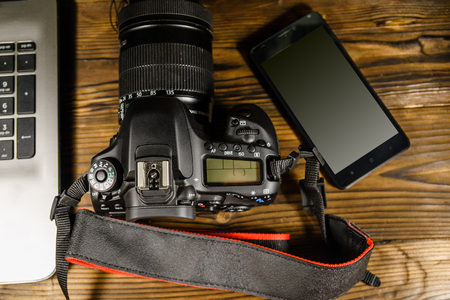 Modern DSLR camera, smartphone and laptop on rustic wooden table. Top viewの写真素材