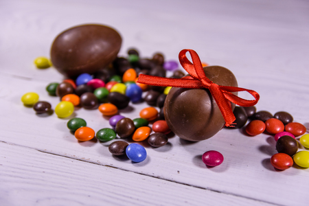 Chocolate easter eggs and multicolored candies on white wooden tableの写真素材