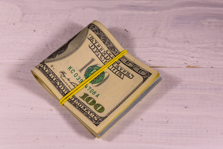 Bunch of the one hundred dollar bills with rubber on white wooden tableの写真素材