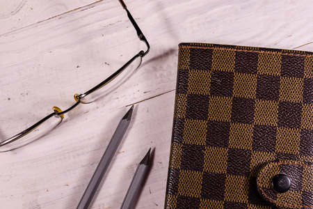 Closed notepad, pencils and eyeglasses on white wooden table. Top viewの写真素材