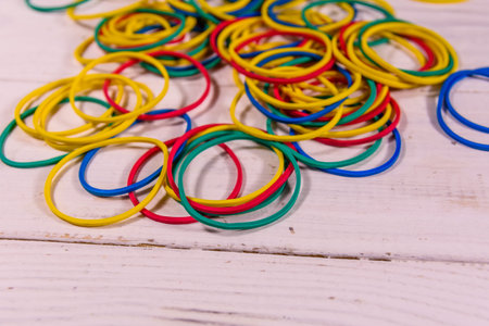 Many multicolored elastic rubbers on white wooden table