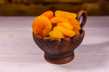 Ceramic bowl with dried apricots on white wooden tableの写真素材