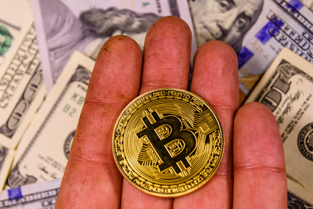 Hand with bitcoin against one hundred dollar billsの写真素材