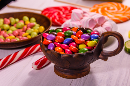 Ceramic bowl with colored candies, candy cane, lollipops and marshmallows on wooden tableの写真素材