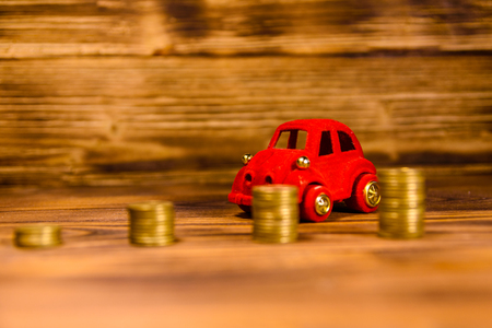 Stacks of the coins and red toy car on rustic wooden tableの写真素材