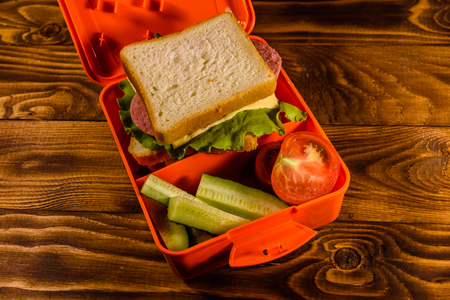 Lunch box with sandwich, cucumbers and tomatoes on rustic wooden tableの写真素材