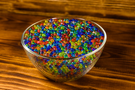 Multicolored hydrogel balls in glass bowl on wooden tableの写真素材