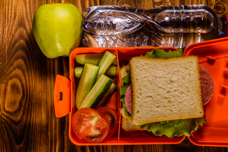 Bottle of water, green apple and lunch box with sandwich, cucumbers and tomatoes on rustic wooden table. Top viewの写真素材