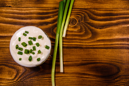 Glass bowl with sour cream and green onion on rustic wooden table. Top viewの写真素材