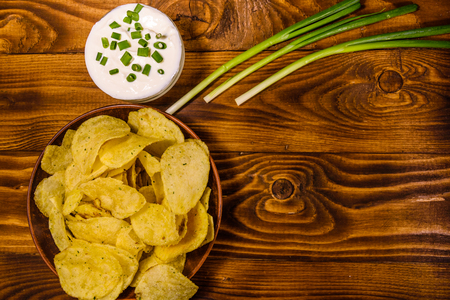 Ceramic plate with potato chips and glass bowl with sour cream on rustic wooden table. Top viewの写真素材