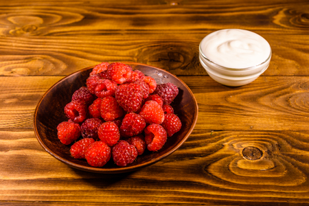 Ceramic plate with ripe raspberries and sour cream on rustic wooden tableの写真素材
