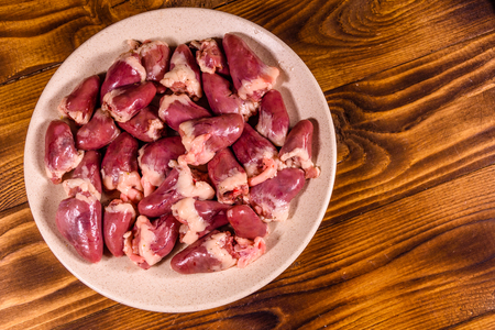 Ceramic plate with raw chicken hearts on rustic wooden table. Top viewの写真素材