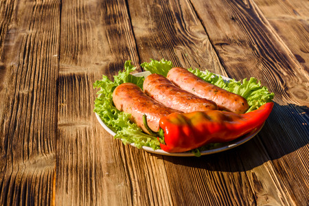 Ceramic plate with grilled sausages, pepper and lettuce leaves on rustic wooden tableの写真素材