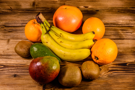Still life with exotic fruits. Bananas, mango, oranges, avocado, grapefruit and kiwi fruits on rustic wooden tableの写真素材