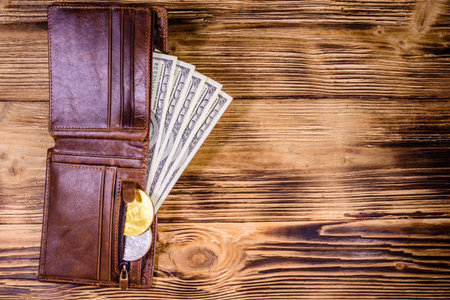 Brown leather wallet, bitcoins and one hundred dollar banknotes on wooden background. Top view
