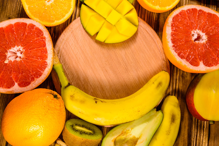 Still life with exotic fruits and cutting board. Bananas, mango, oranges, avocado, grapefruit and kiwi fruits on rustic wooden table. Top viewの写真素材
